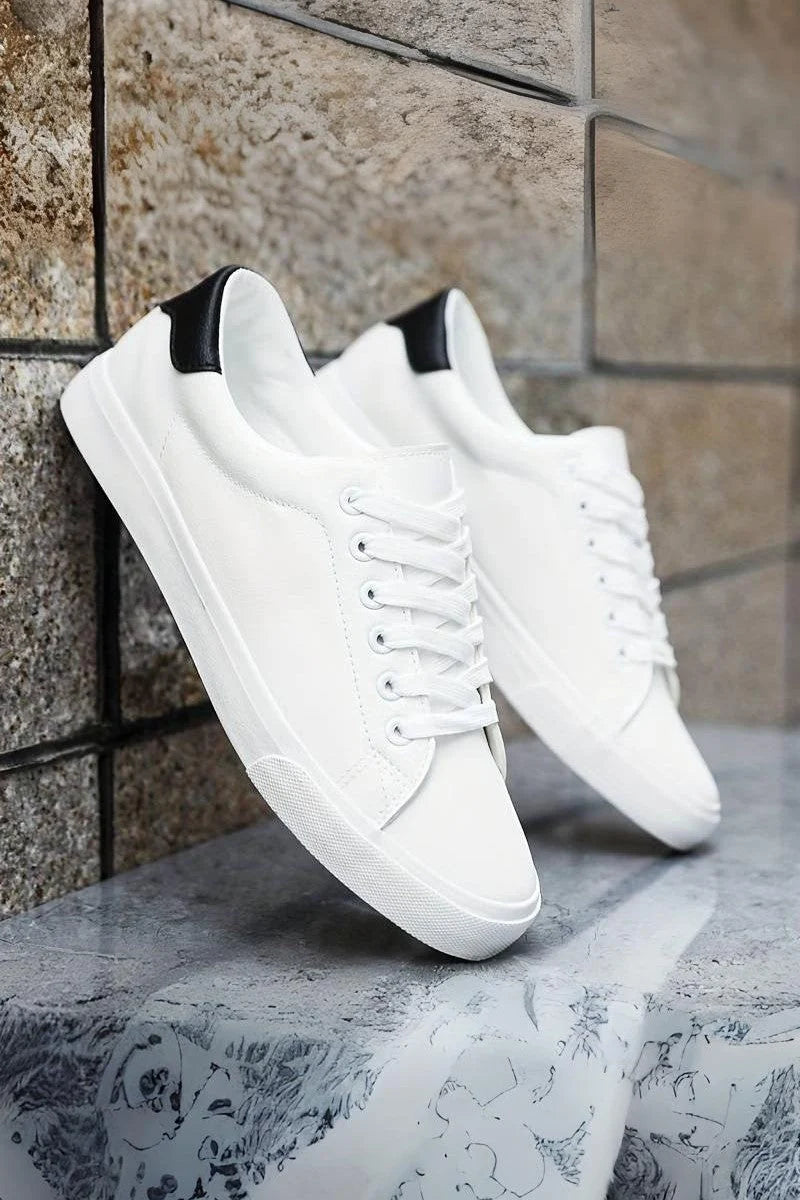 Białe sneakersy męskie minimalistyczne z czarnym panelem na pięcie, sznurowanie, gładka powierzchnia, zaokrąglony czubek, widok z boku.