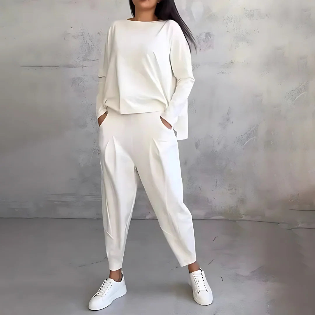 Dwuczęściowy dres damski w kolorze białym z bluzą i spodniami na modelce stojącej na tle szarej ściany